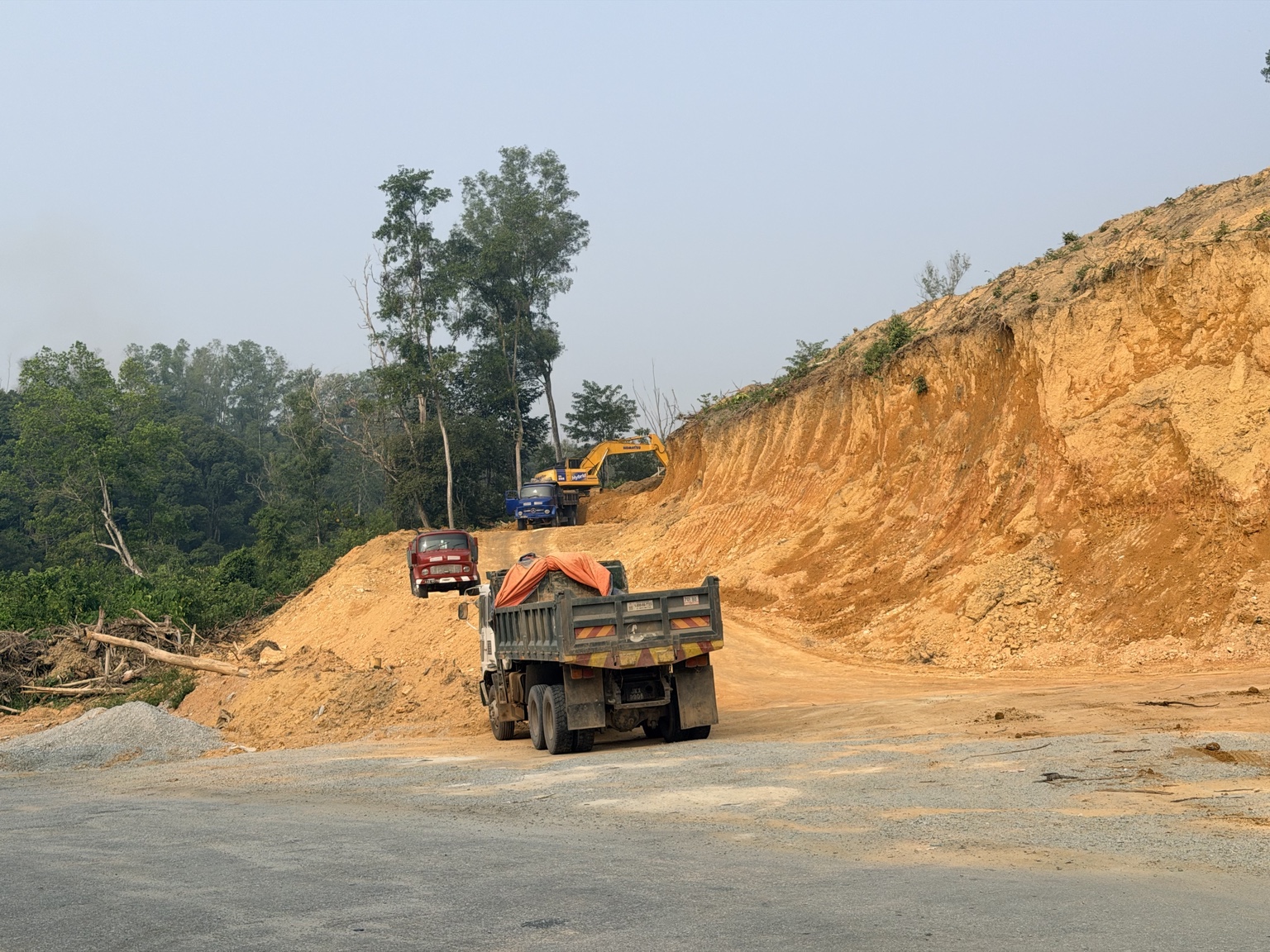 Lorries and an excavator at a red earth loading area